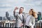 Two young business people with smartphone standing on a terrace, taking selfie.