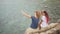 Two Young Carefree Hipster Girls Making Selfie Photo with Mobile Phone and Sitting on Rocks near Sea. HD Slow Motion