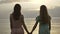 Two young Caucasian girls in dresses walking along shallow water at sunset, turn around and look at the camera