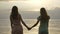 Two young Caucasian girls in dresses walking in shallow water at sunset