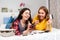 Two young Caucasian women are lying on the bed and cheerfully watching something on their smartphone, holding a Bank card. The