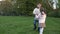 Two young children, an older boy and a younger girl, twirl around holding hands on the park lawn. The children are in