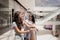 Two young cute thin dark-haired girls,stand next to each other in a modern mall.