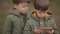 Two young cute twin boys wear green Spring jackets use mobile phone to watch cartoons. Smarthphone addiction concept
