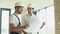 Two young engineer in a safety helmets standing at building site holding a blueprint of the structure. Construction