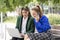 Two Young Executive Women Working Sitting on a Street Bench Using Their Laptop and Calling on Cell Phones