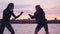 Two young female fighters train on the street against the background of a river in the city at sunset. Boxers, sports