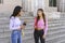 Two young female university students leaving the university and chatting smiling and funny on the staircase. Concept of friendship