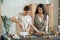 Two young females standing by table while one of them cutting hard soap mass