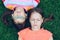 Two young girls lying on the grass with their eyes closed on their backs and listening to music