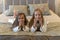 Two young girls are lying in white bathrobes on a bed in a hotel. Children sisters on vacation