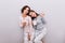 Two young girls in pajamas with cups on gray wall background. Girl with long hair lean head on shoulder of girl with