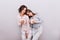 Two young girls in pajamas with cups on grey wall background. Girl with long hair lean head on shoulder of girl with