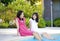 Two young girls sitting by swimming pool, smiling