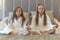 Two young girls are sitting in white bathrobes on a bed in a hotel and meditating. Lotus position