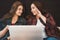 Two young girls or women laughing and discussing something using laptop, female lesbian couple spend time together