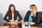 Two young girls working in an office, making a paper airplane, and the second with hatred looks at her