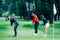 Two young golfers practicing chipping shots on a golf course with golf instructor