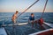 Two young handsome men at the aft of the sailboat preparing for diving, captain driving yacht in sea at sunny day