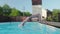 Two young happy blondes synchronously dive into outdoor pool. Slowmo