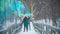 Two young happy women having fun on the snowy bridge holding colorful smoke bombs