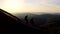 Two young hikers with backpacks descend a rocky ridge at sunset.