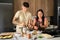 Two young latin people mashing potatoes and grating tomato at kitchen.