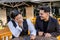 Two young Latinos at an outside table in a bar talking and having fun. One of the young men takes his head