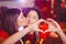 Two young lesbian girls kiss and make a heart with their hands at a club party