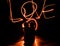 Two young lovers paint a heart on fire. Silhouette of couple and Love words on a dark background