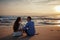 Two young lovers sitting on a beach and looking to each other on sunset background.sillhouette couple love.Romantic and