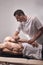 Two young man, 20-29 years old, sports physiotherapy indoors in studio, photo shoot. Therapist masseur massaging arm of muscular