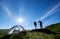 Two young people in backpacks and trekking sticks give each other high five near camping in mountains