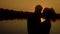 Two young people hugging against the backdrop of a sunset by the river, close-up, slow motion
