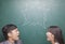 Two young people yelling at each other in front of blackboard, symbol on chalkboard