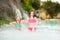 Two young sisters bathing in natural swimming pool in Bagno Vignoni, with thermal spring water and waterfall. Tuscany, Italy