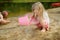 Two young sisters having fun on a sandy lake beach on warm and sunny summer day. Kids playing by the river