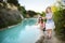 Two young sisters playing by natural swimming pool in Bagno Vignoni, with thermal spring water and waterfall. Tuscany, Italy