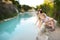 Two young sisters playing by natural swimming pool in Bagno Vignoni, with thermal spring water and waterfall. Tuscany, Italy