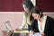 Two young smartly dressed women filling out forms at a vintage office desk in front of a laptop