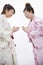 Two young smiling woman in Japanese kimonos bowing to each other, studio shot