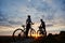 Two young sports people on mountain bikes stand on rock at top of hill looking for sunset