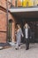 Two young stylish women in medical masks talking and laughing while walking the street in town. Friends strolling