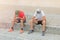 Two young teenagers sitting on the stone pavement playing and chatting on social networks with their mobile phone with their