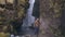 Two young tourists exploring the powerful waterfall Gljufrabui in Iceland. Man and woman in raincoat walking in rain.