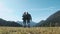 Two young travellers walking back in front of grass. Couple trekking and holding hands with view of mountains. Man and
