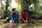 Two young trekkers or traveler sits on rocks in mountain river and enjoys with mountain stream water in hands while washing face