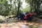 Two young trekkers or traveler sits on rocks in mountain river and enjoys with mountain stream water in hands while washing face