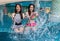 Two young woman friends splashing water in swimming pool