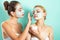 Two young women applying moisturizer cream on their face. Photo of careful friends receiving spa treatments. Home